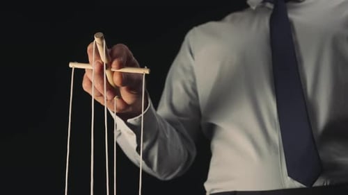 Un hombre de negocios con camisa blanca y corbata negra controla una marioneta con un manipulador de madera y cuerdas