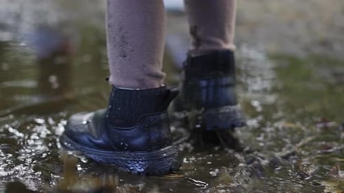 Toddler splashing her black boots in the big muddy puddle, autumn forest.