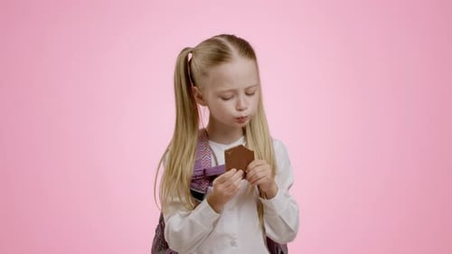 Adorable Little Schoolgirl with Backpack Biting Chocolate Bar Enjoying Sweet Snack for Lunch and
