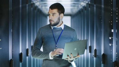 Männlicher Serveringenieur arbeitet an einem Laptop im Rechenzentrum und lächelt dann.