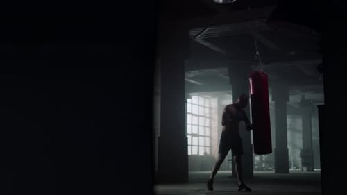 Man Boxing a Punching Bag in Dark Gym