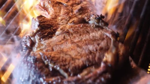 Rindersteak auf dem Grill mit Feuerflammenfleisch Rindersteak auf dem Grill Nahaufnahme Barbecue-Grill Rohes Rindersteak