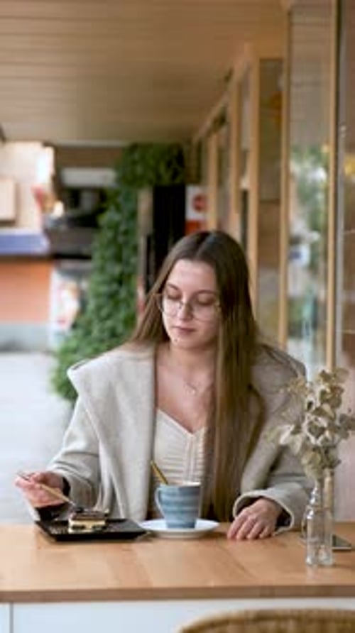 Woman Eating a Cake and Drinking Coffee in a Cafe