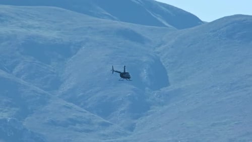 Helicopter Flies Over Mountain Landscape on Sunny Day