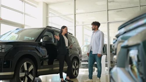 Saleswoman Showing New Black Car to Customer in Dealership