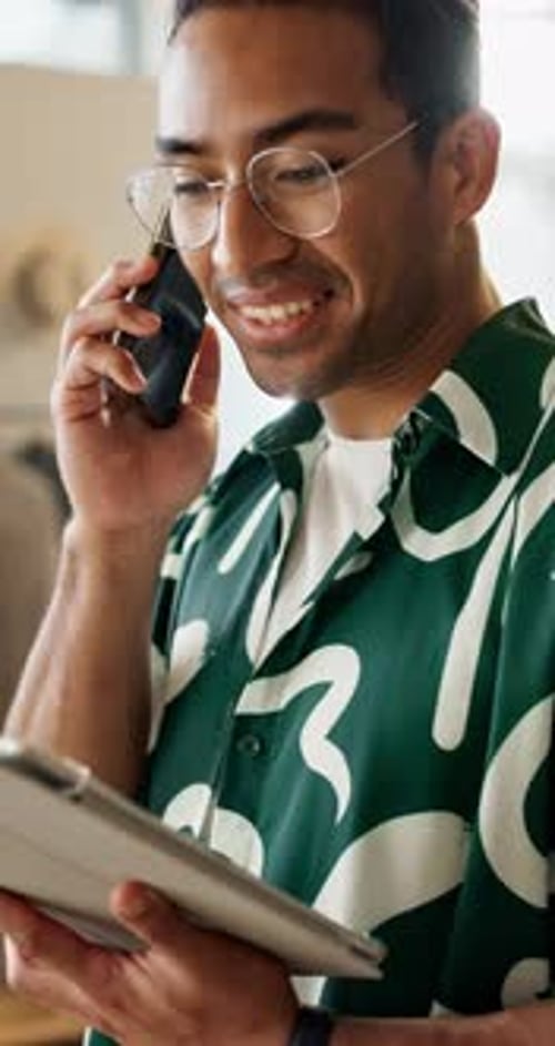 Young Adult Talks on Phone While Looking at Tablet