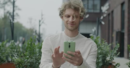 Portrait of Joyful Young Man Using Smartphone Browsing and Using Social Media Outdoors in City on