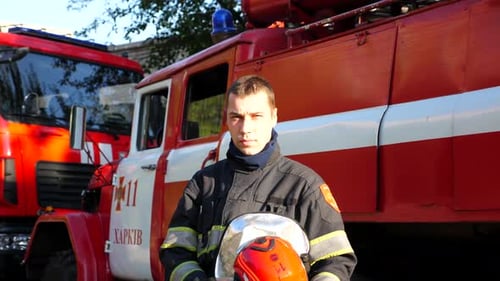 Firefighter in Uniform Stands in Front of Firetrucks