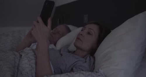 Mujer adulta mayor mirando su teléfono inteligente en el dormitorio por la noche antes de dormir, insomnio