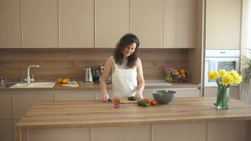 Woman with Headphones Cuts Cucumber for Salad