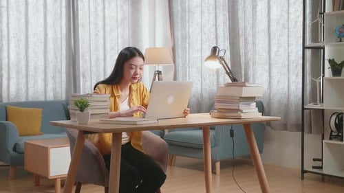 Woman Works on Laptop at Table with Books