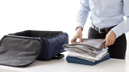 Man packing blue suitcase with folded clothes indoors