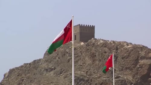 Deux drapeaux de l'État d'Oman ondulant dans le vent : à l'arrière, vous pouvez voir la tour de la forteresse.