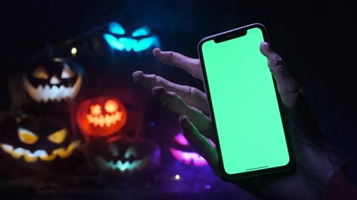 Creepy skeleton hand holding a phone with green screen at a party during Halloween