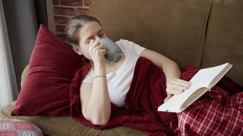 Woman Relaxing on Couch Drinking Tea and Reading