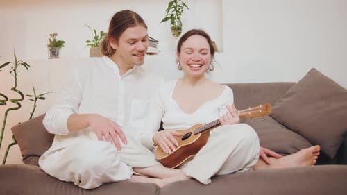 Affectionate Couple Sitting on Sofa Playing Ukulele
