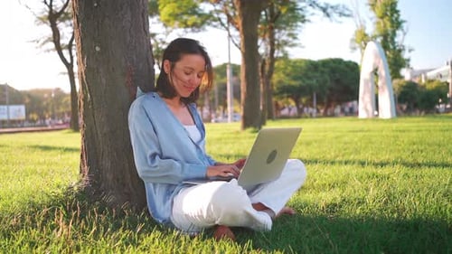 Woman with Laptop Sits Under a Tree