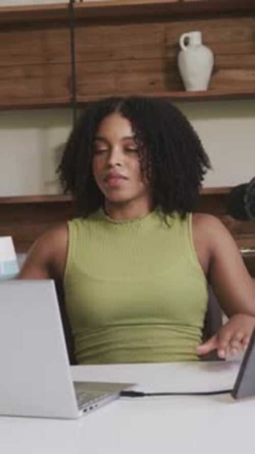 Vertical video: Drinking woman in green top sipping from blue mug while working at laptop in studio