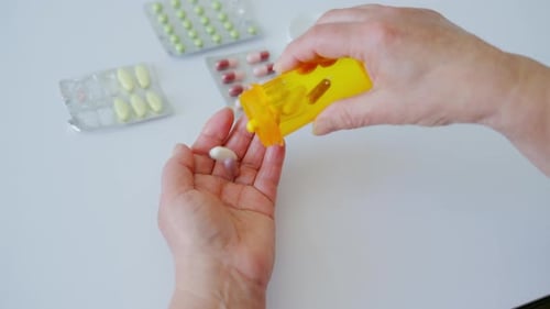 Close Up of Elderly Hands Pouring Pills From an Orange Prescription Bottle Into the Palm with