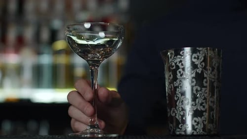 Close up of a bartender putting ice cubes into the small empty cocktail glass