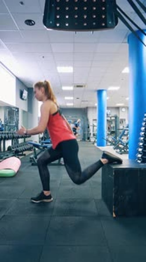 Woman doing squats in the gym. Girl in sportswear squats with obstacle in the modern fitness center.