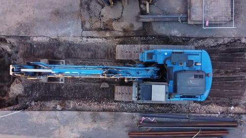 Excavator from above on a construction site in city. Ascending top down drone shot of industrial equ
