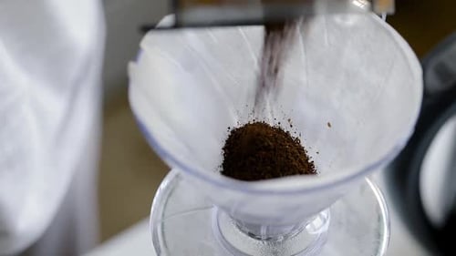 Coffee Grounds Pouring into Paper Coffee Filter