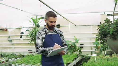 Gardener Taking Notes in Greenhouse Surrounded by Plants