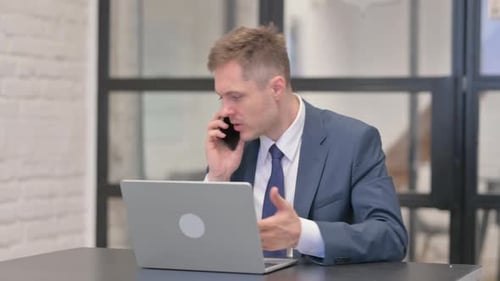 Man in Suit Uses Laptop and Mobile Phone