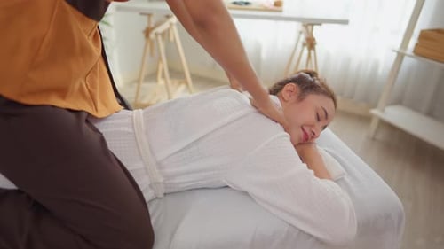 Beautiful woman in bathrobe getting back massage treatment at beauty spa.