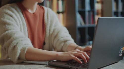 Asian Female Student Typing on Laptop at Desk in Library