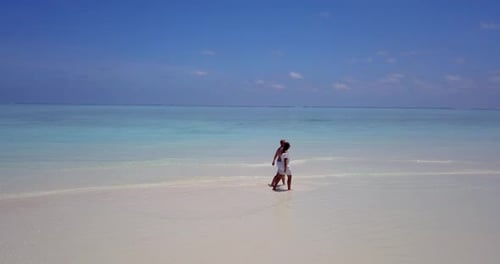 A follow up aerial shot of a couple holding their hands and walking together along the beach in Mald