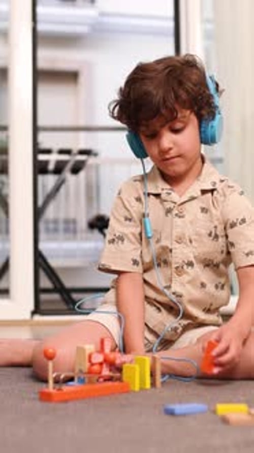 Cute Child Playing with Blocks at Home Wearing Headphones