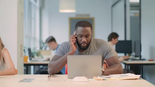 African businessman works on laptop and talks on mobile phone in coworking space