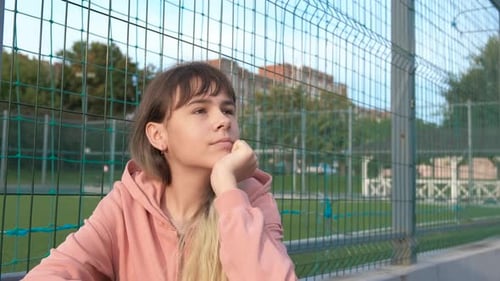 Teen Sits in Front of a Green Fence