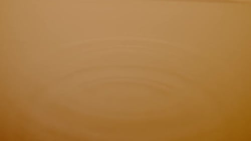 Macro Shot of a Drop of Water Falls on Brown Liquid Surface Creating Water Rings and Waves