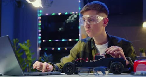 Teen Engineering a Toy Car with Laptop