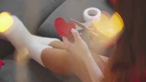 Woman Cutting a Red Heart on Gray Couch