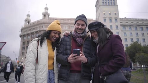 Three Happy Friends Talking About Smart Phone Content in Winter in the Street