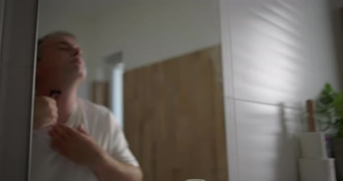 Homem olhando para o espelho enquanto se barbeia debaixo do pescoço, limpe movimentos precisos com navalha, natural