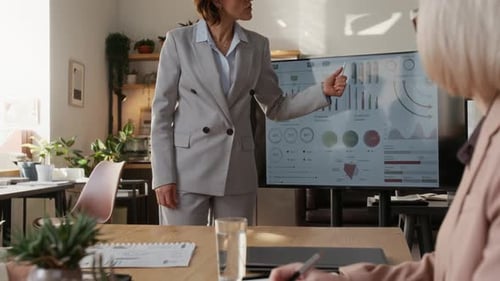 Woman Presenting Business Charts and Data to her Colleagues at Desk in Office