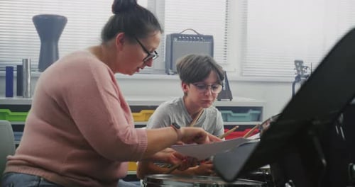 Boy Receives Drum Lesson from Woman in Music Classroom