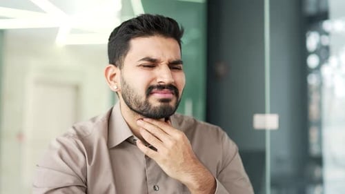 A sick businessman suffering from a sore throat while sitting at a workplace in a business office.