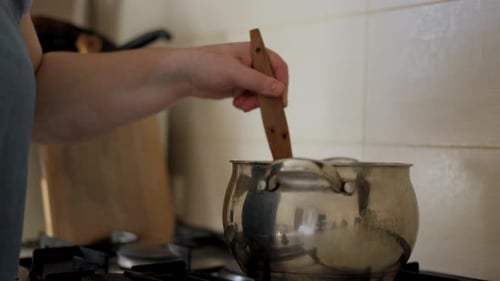 Female hands stir the jam with a wooden spoon. The process of making apricot jam.