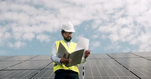 Techniker steht mit Dokumentenmappe und überprüft Sonnenkollektoren im Freien