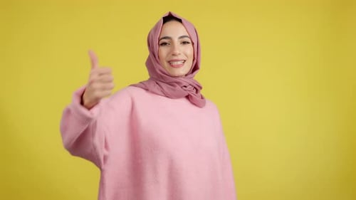 Glückliche muslimische Frau gestikuliert zustimmend und hebt den Daumen hoch