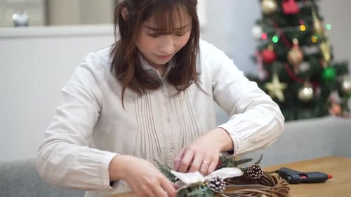 Woman Decorates Christmas Wreath with Holiday Ornaments