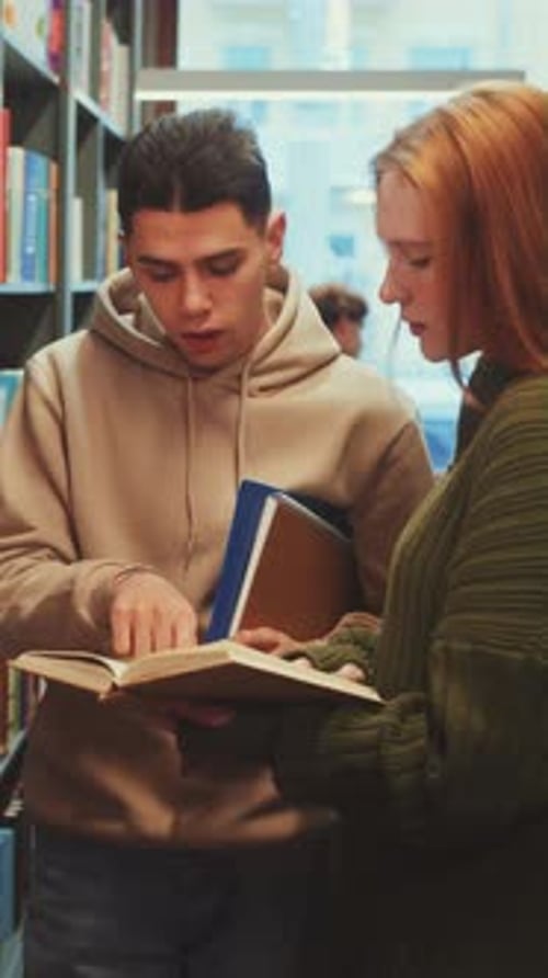 Vertical Screen Two Students Discussing a Book in a Library Aisle