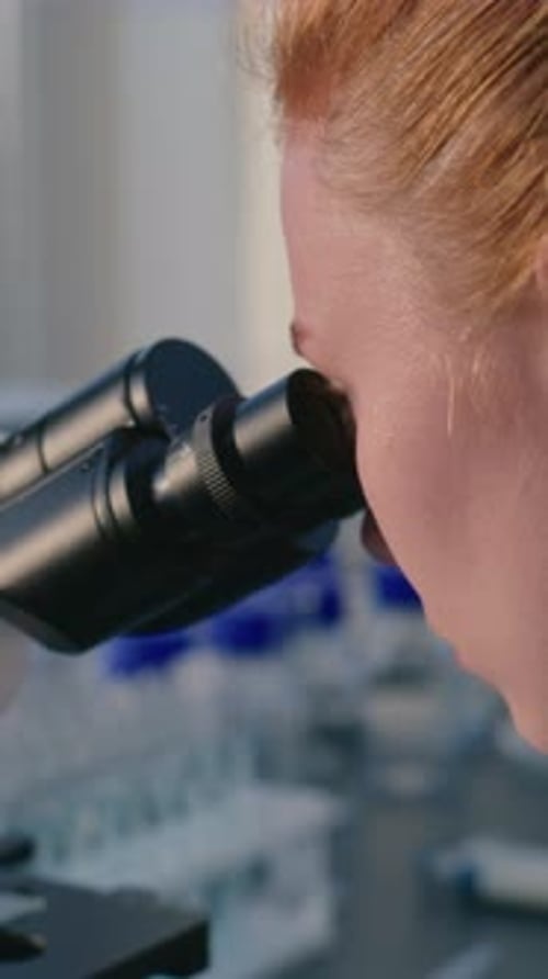 Close Up of Female Microbiologist Looking Under Microscope Analyzing Test Sample