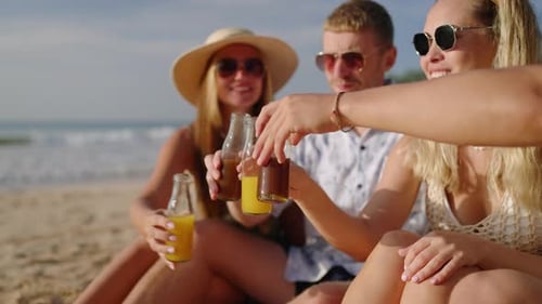 Quatre amis joyeux sont assis sur une plage de sable, boivent du kombucha et discutent lors d'une visite tropicale en riant
